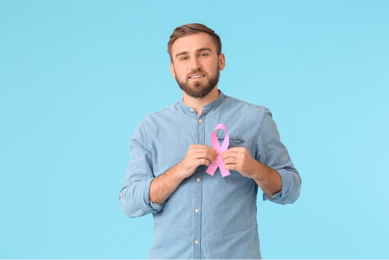 Imagem de um homem segurando uma fita que faz alusão a prevenção ao câncer de mama.